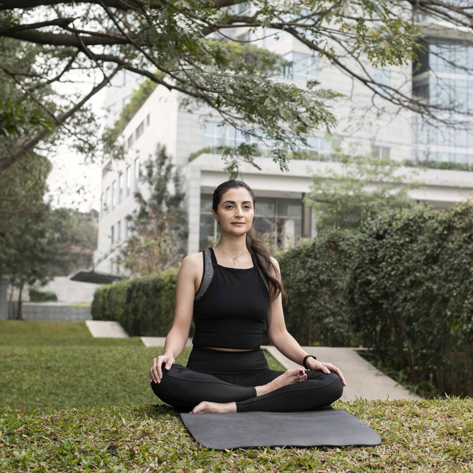 Person wearing athletic clothes and sitting on a yoga mat with their legs crossed.