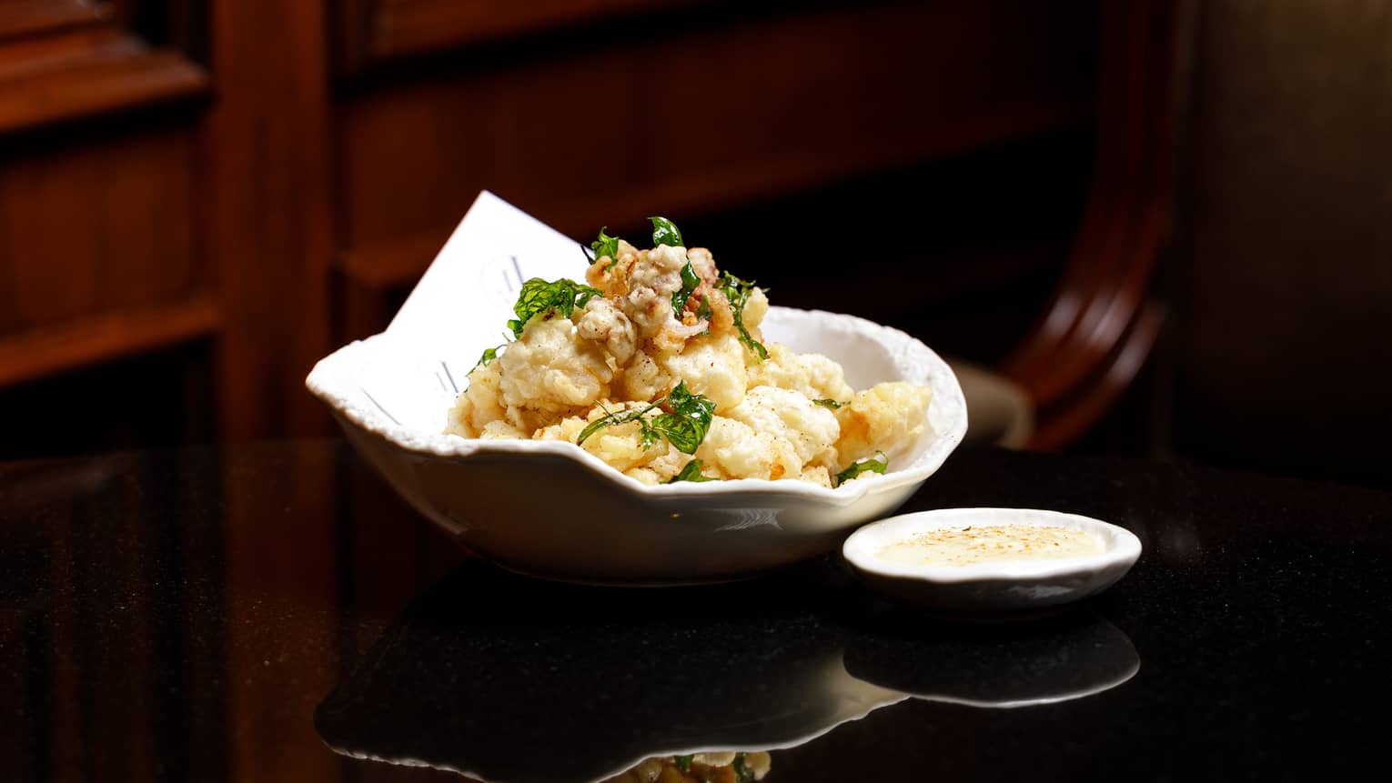 Calamari in a white bowl with a side of dipping sauce