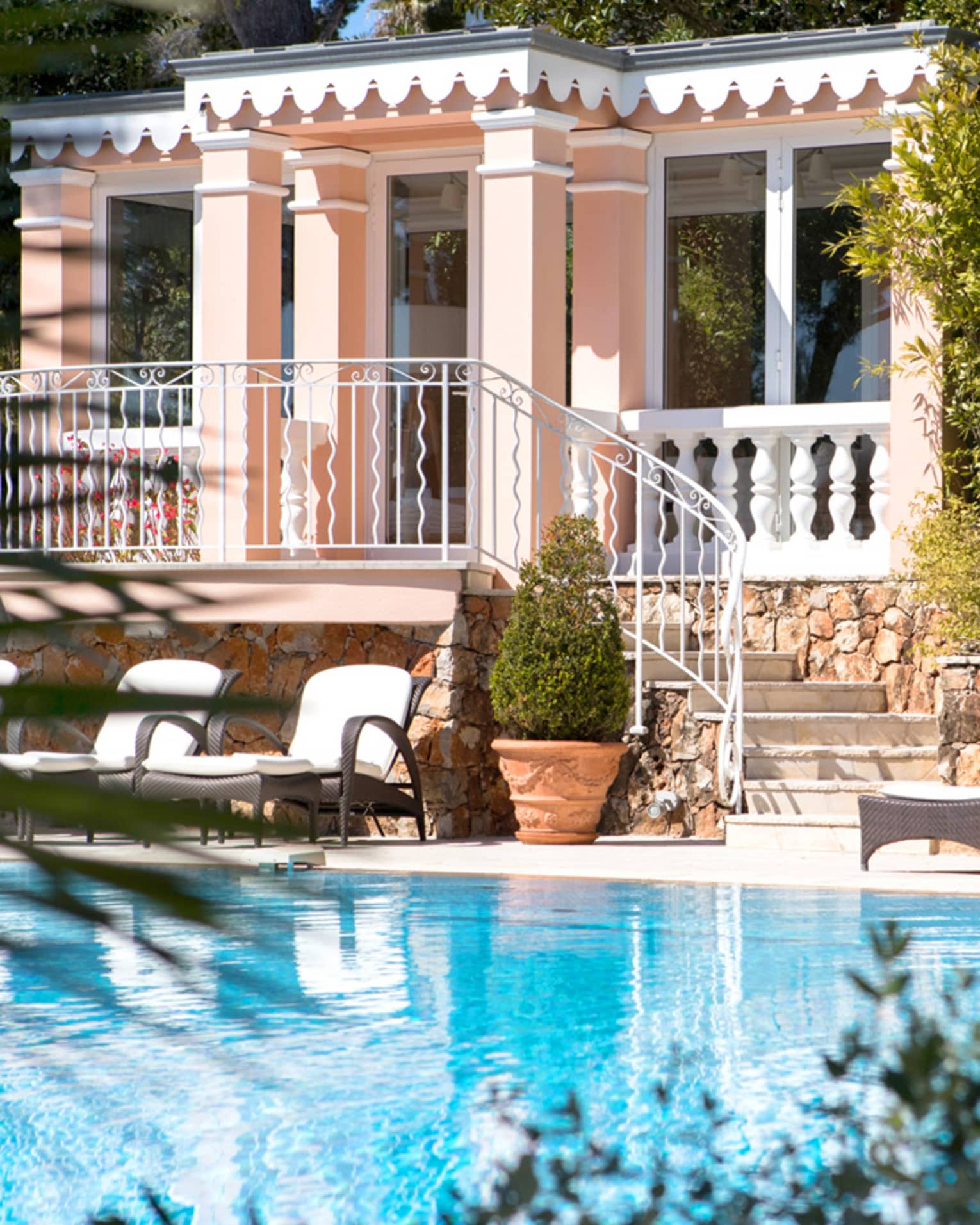 Pristine pool, lounge chairs and umbrella in front of large three-storey pink Villa Rose-Pierre