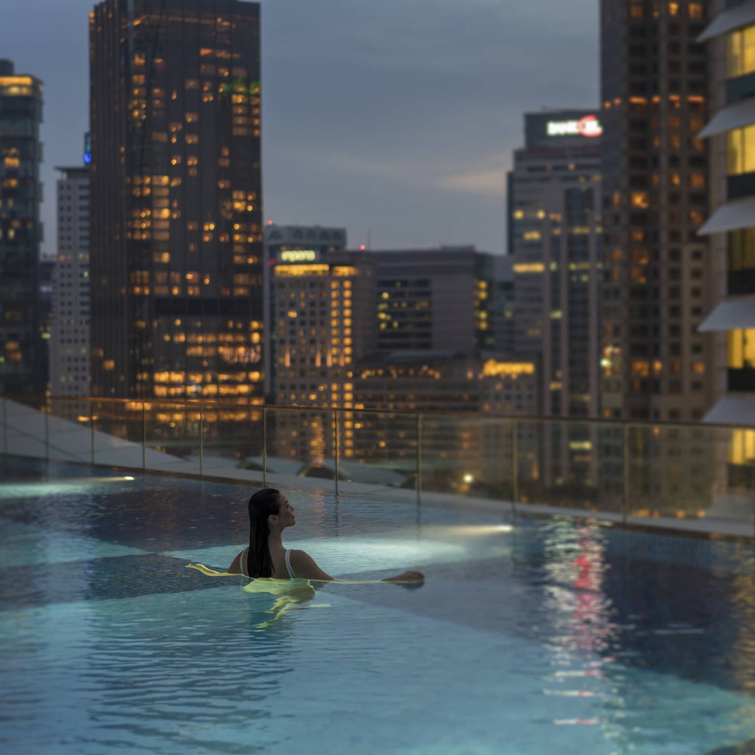 A woman swims in an infinity pool with a view of the city skyline