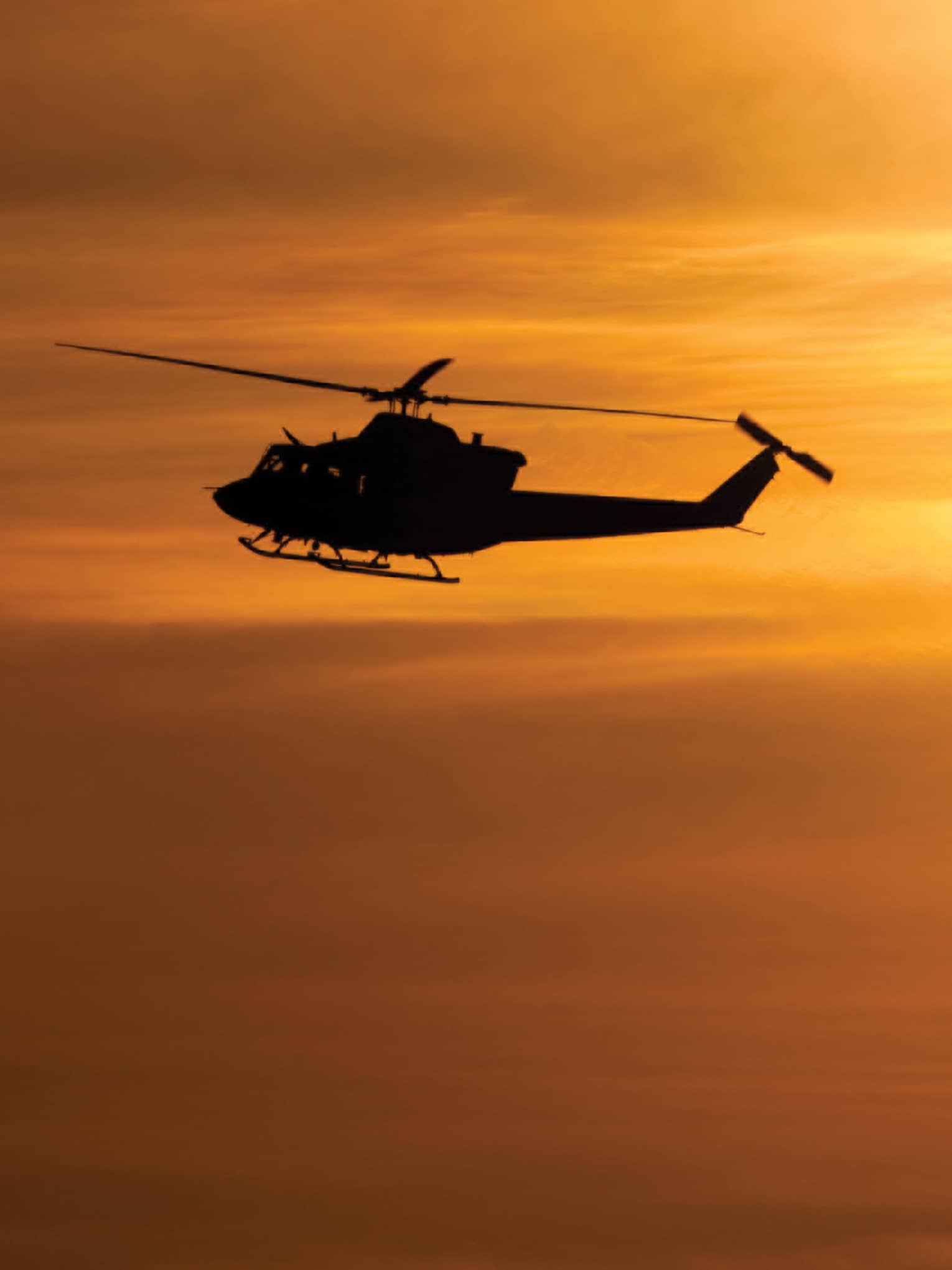 Silhouette of helicopter against orange sky