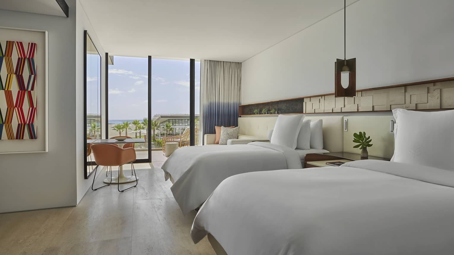 Two Bedroom Ocean View Suite with two Double beds, white linens, small round table, floor-to-ceiling window with Resort views and two-tone curtains