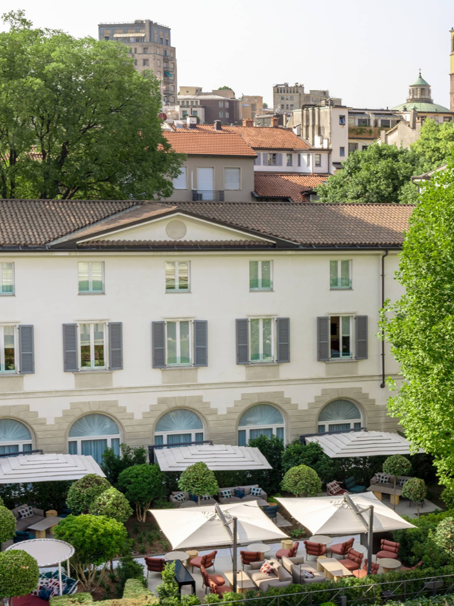 Aerial view of lush courtyard at Four Seasons Hotel Milano, with outdoor dining, umbrellas, manicured trees