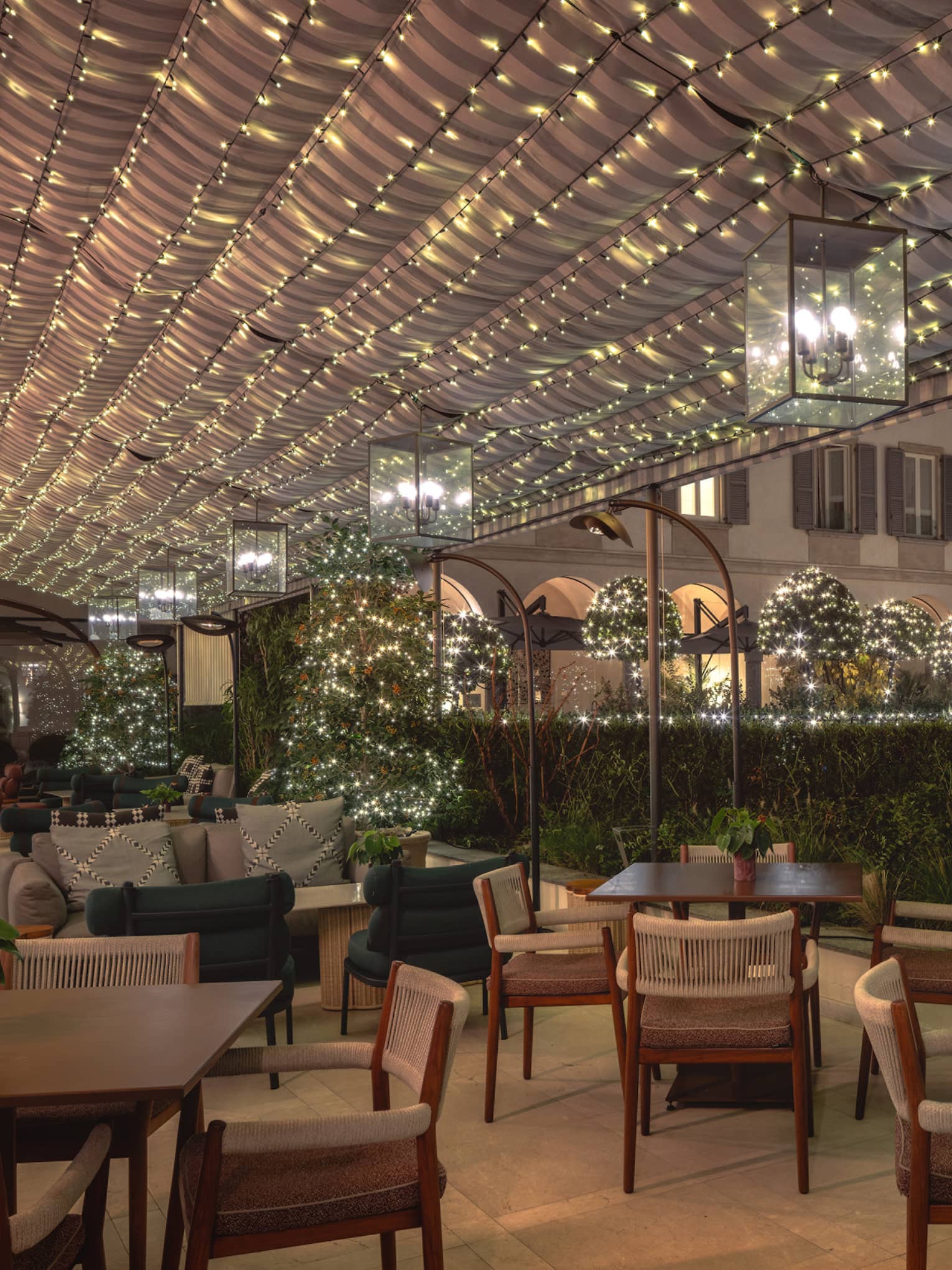An outdoor dining area with holiday decor, including strings of holiday lights overhead