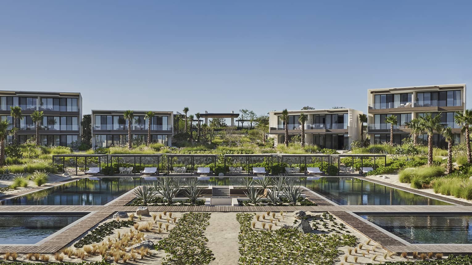 A large pool made of many smaller square pools, a large building and plants surround the pool.