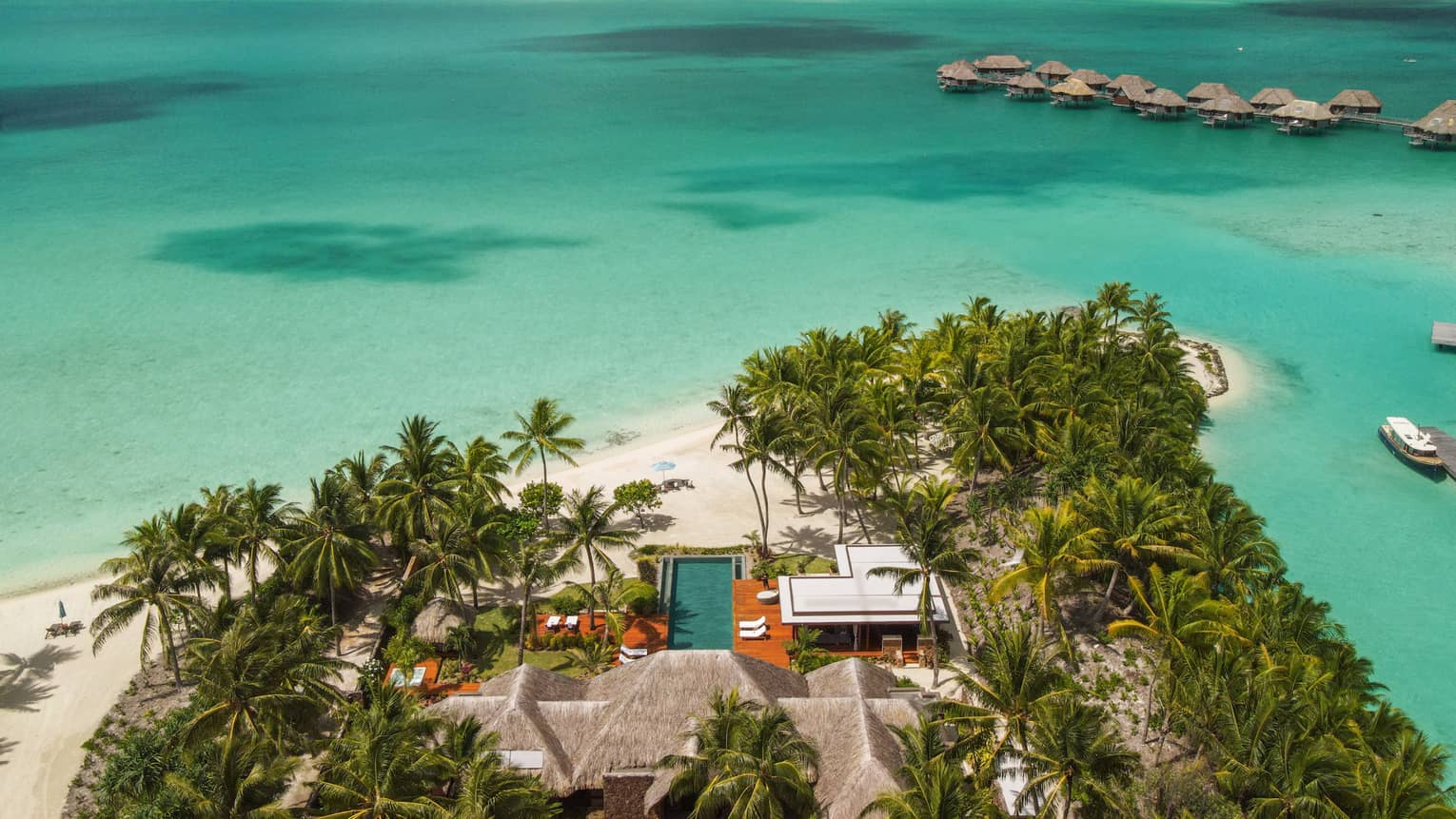 Aerial view of Bora Bora villa on edge of turquoise lagoon, looking out to overwater bungalows and mountains