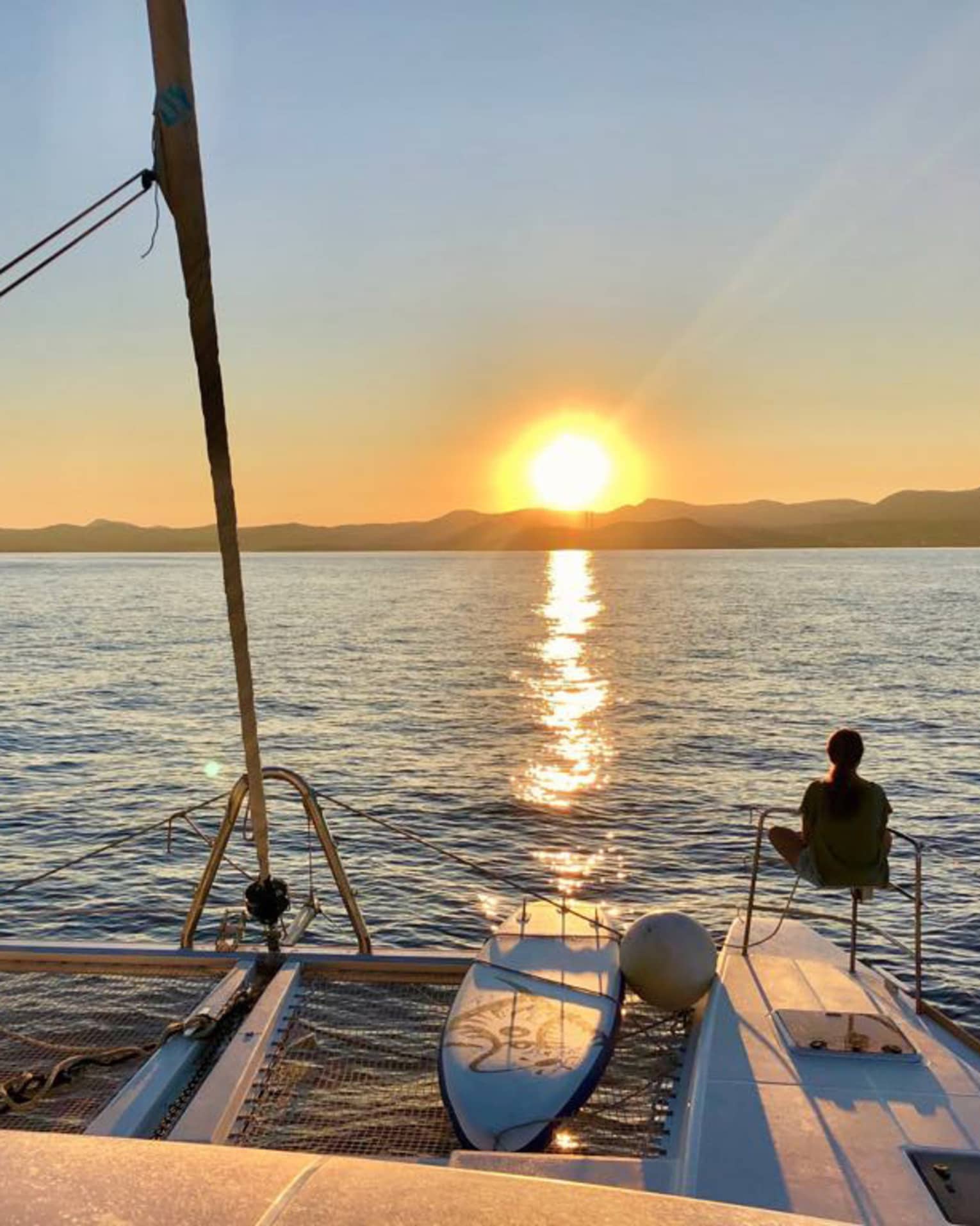 Two guests lounge on luxury sailboat near stern railing at sunset