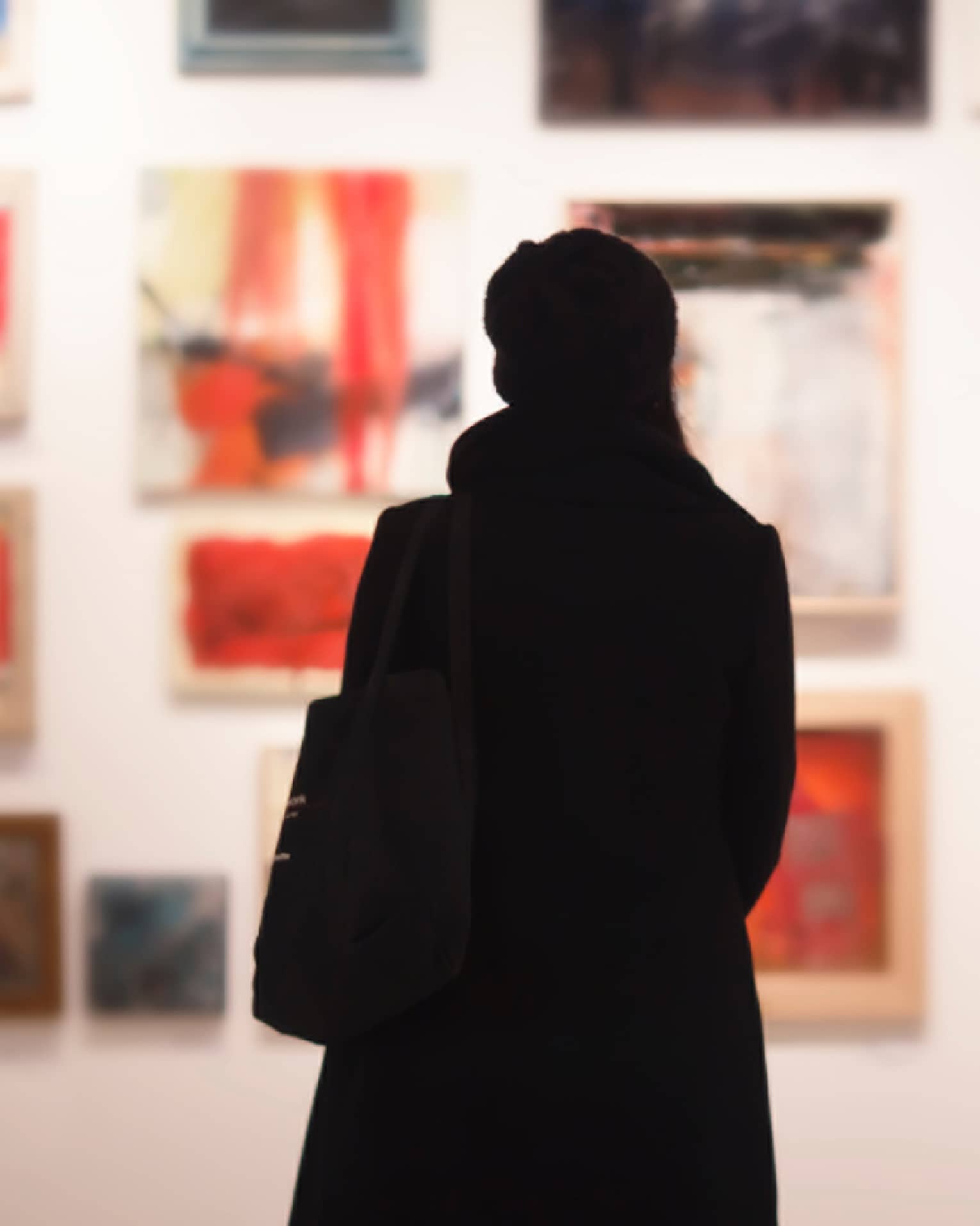 Silhouette of back of woman with hat bag looking at gallery wall with colourful art