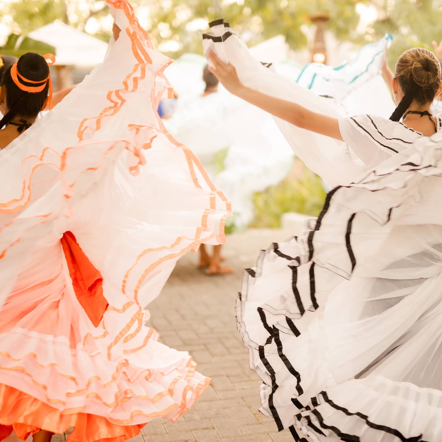 Two women dressed in multi-layered dresses with ruffls along the hem dance on a patio