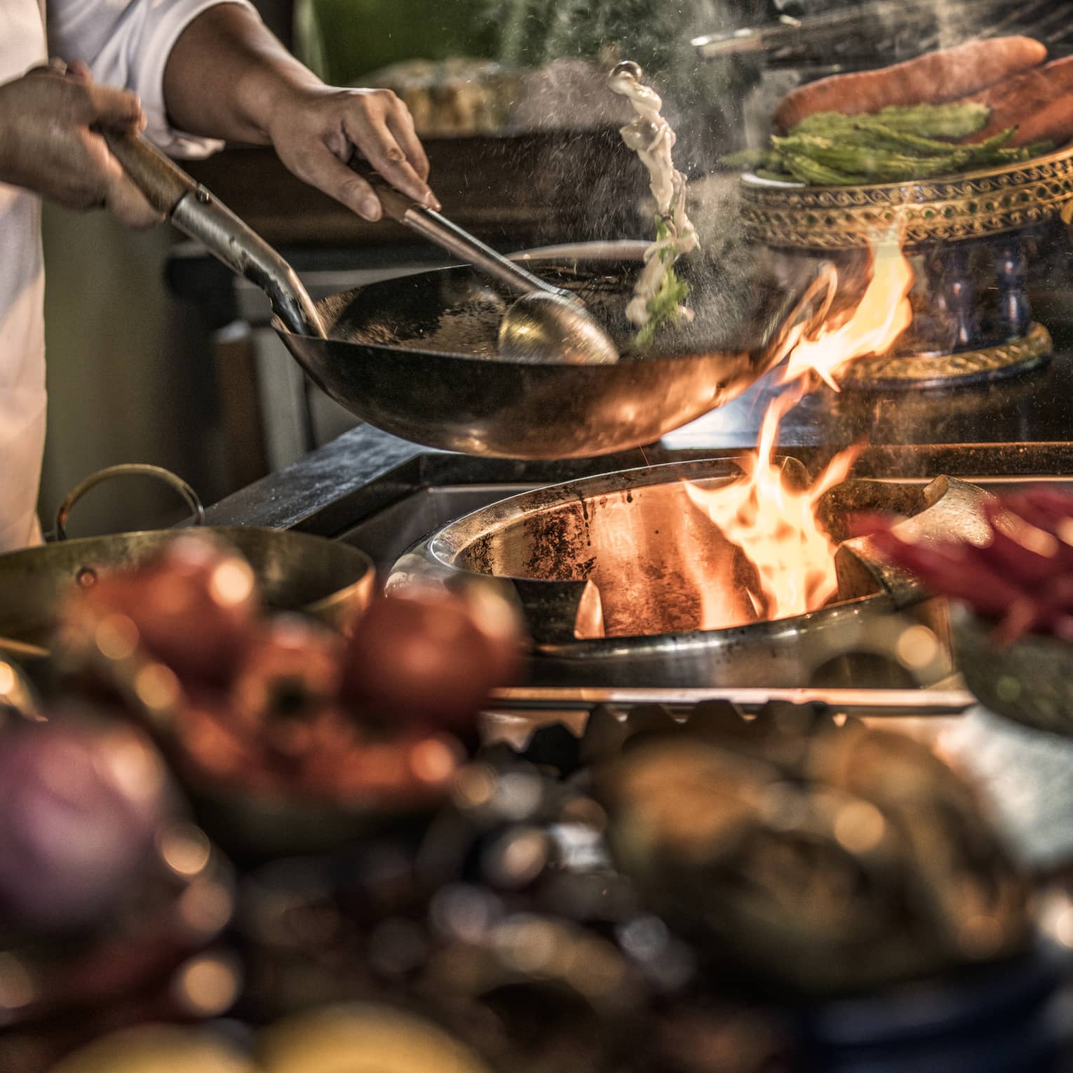 Close-up of chef stirring meals in copper pans over stove, flames
