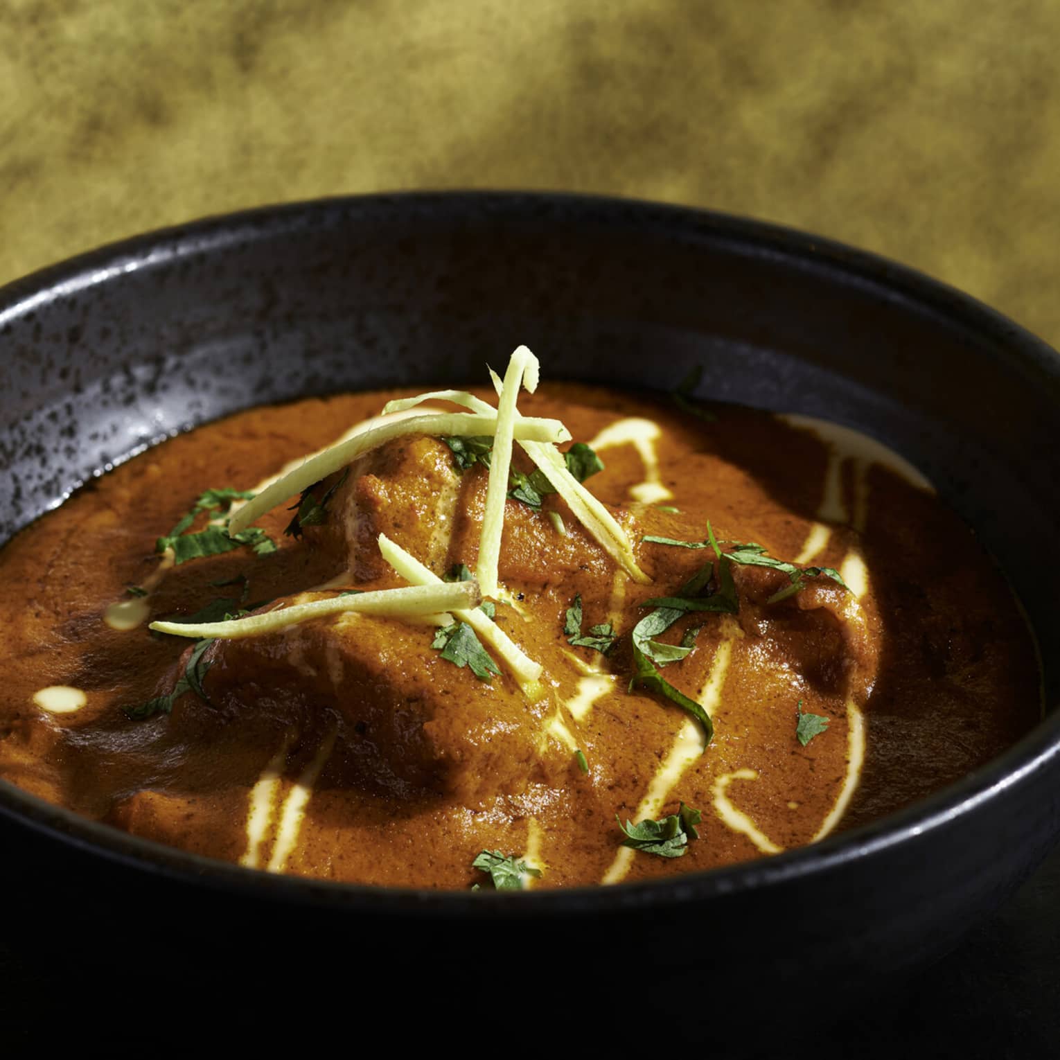 Bright red Tandoori dish with chicken, fresh herb garnish in black earthenware bowl