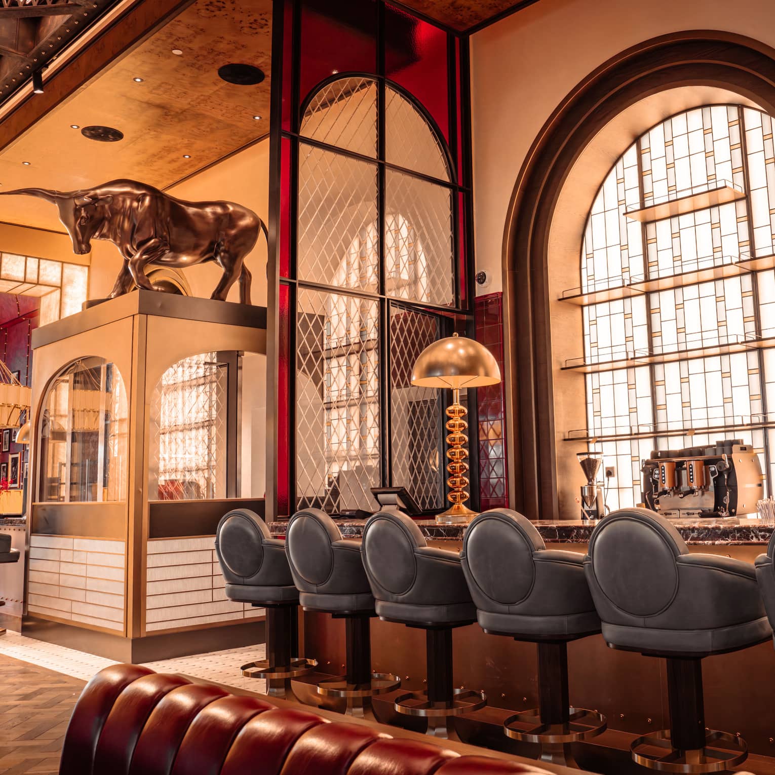 Bar area of a restaurant featuring blue leather bar stools, large brass lighting and 1920s-style decor