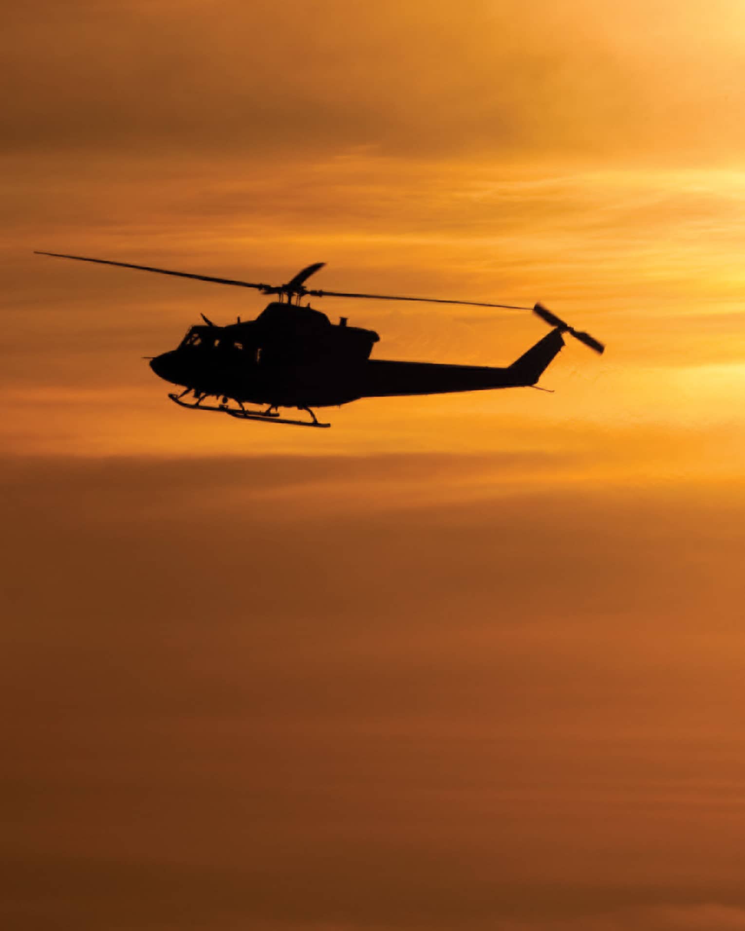 Silhouette of helicopter against orange sky