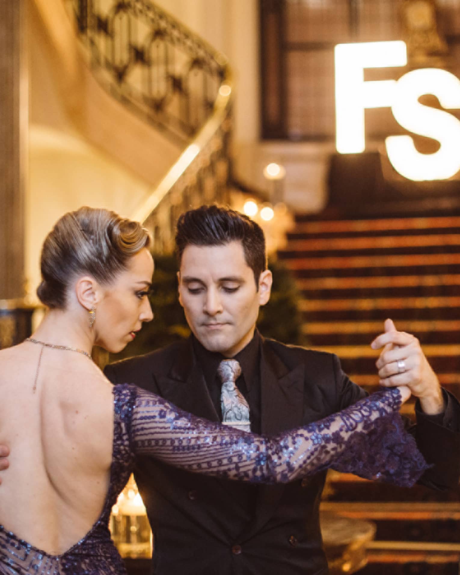 A man and woman tango dancing at the bottom of a wide red carpeting stairway