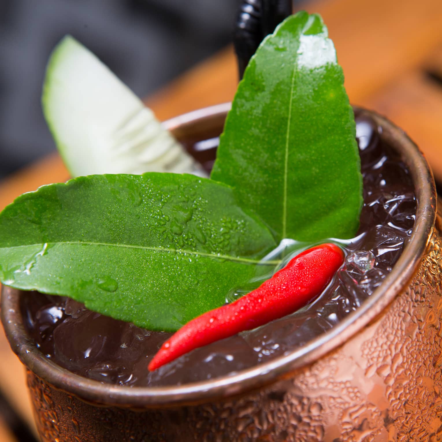 Close-up of green lime leaves, small red hot pepper on cocktail in brass cup