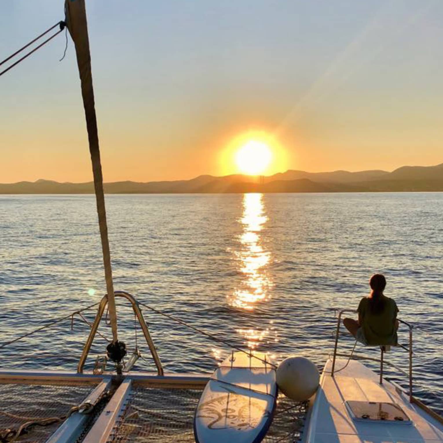 Two guests lounge on luxury sailboat near stern railing at sunset