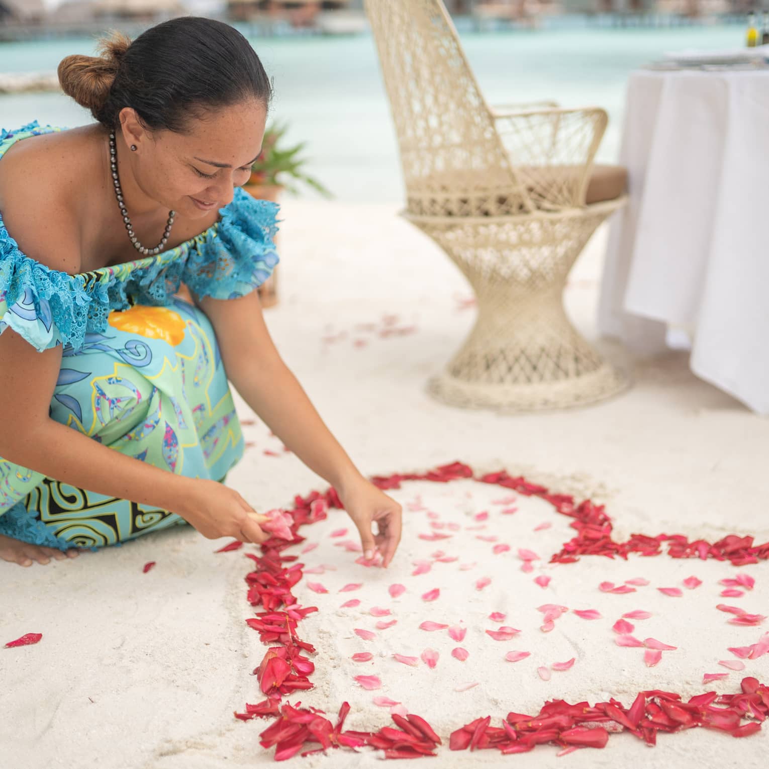 Woman arranges red rose petals into heart shape on sand beach