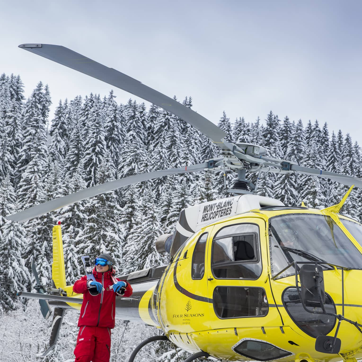 A yellow helicopter rests atop a snow covered mountain in Megeve