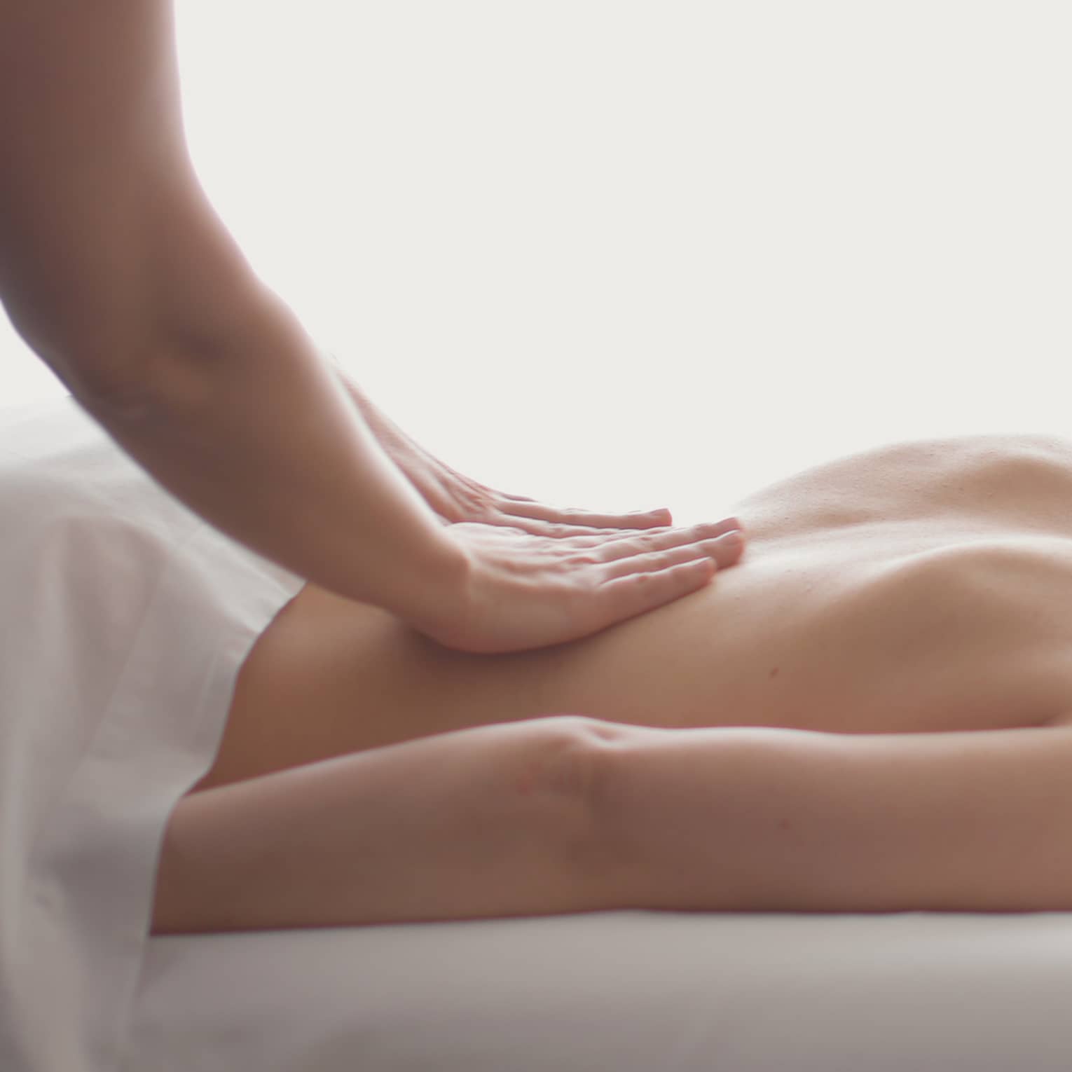 Side view of woman lying on massage table, hands massaging her bare shoulders