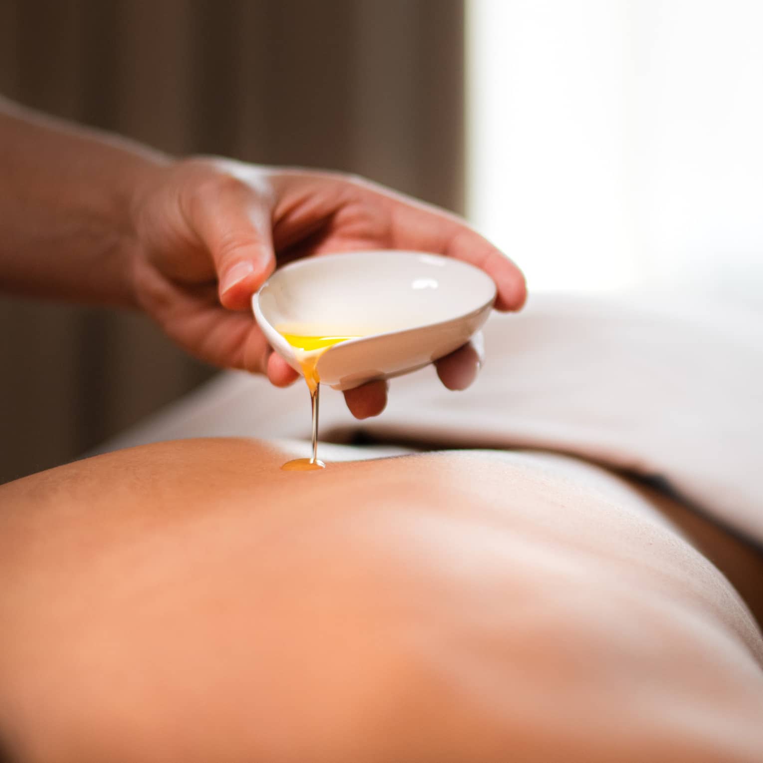 A spa staff member pouring liquid onto a woman?s back.