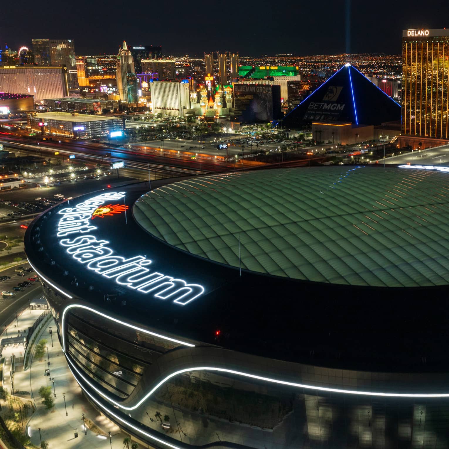 A nighttime, birds-eye view of a large sports stadium, with other tall buildings and lights around it.