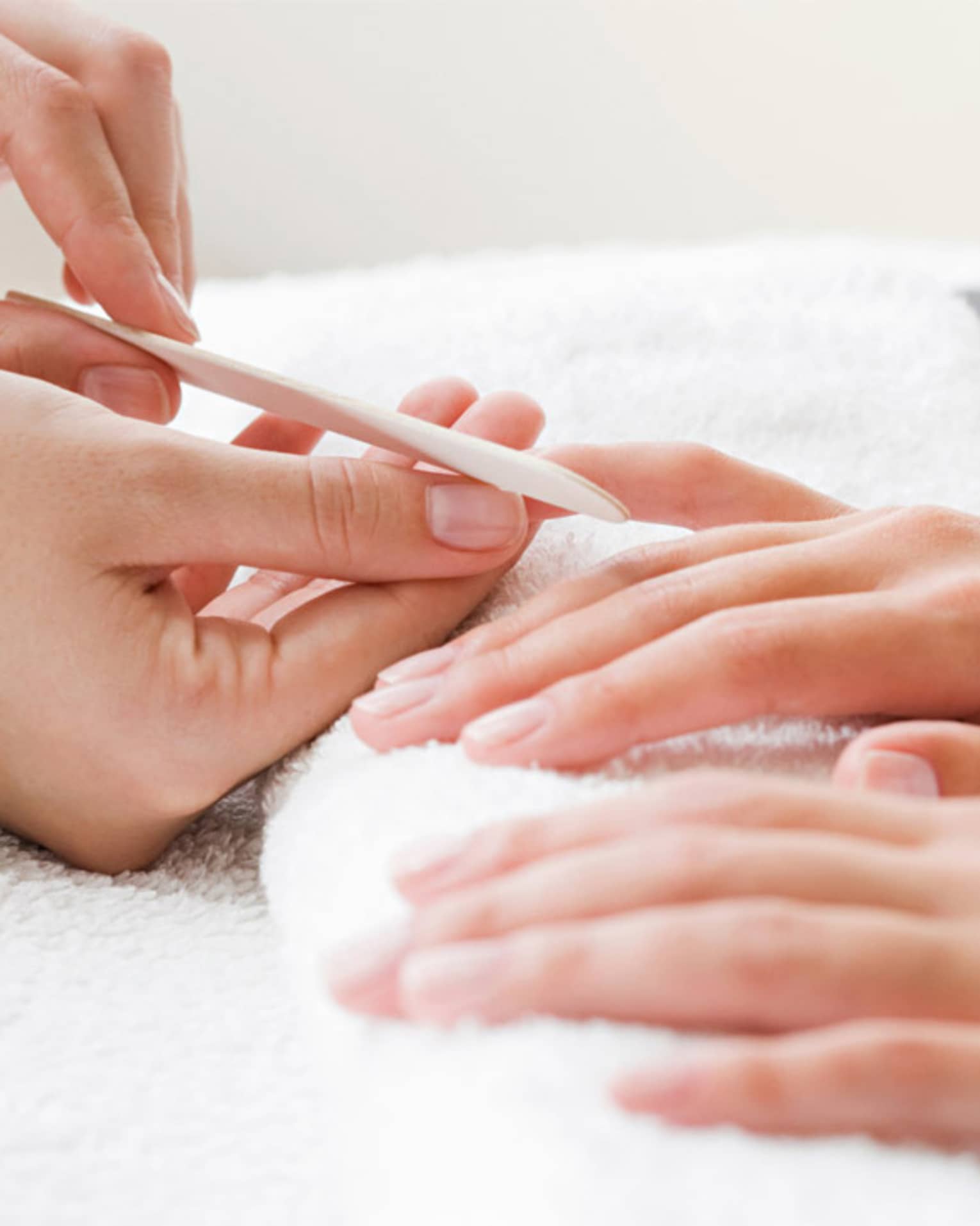 Close-up of spa attendant filing nails of woman's hands as they rest on white towel