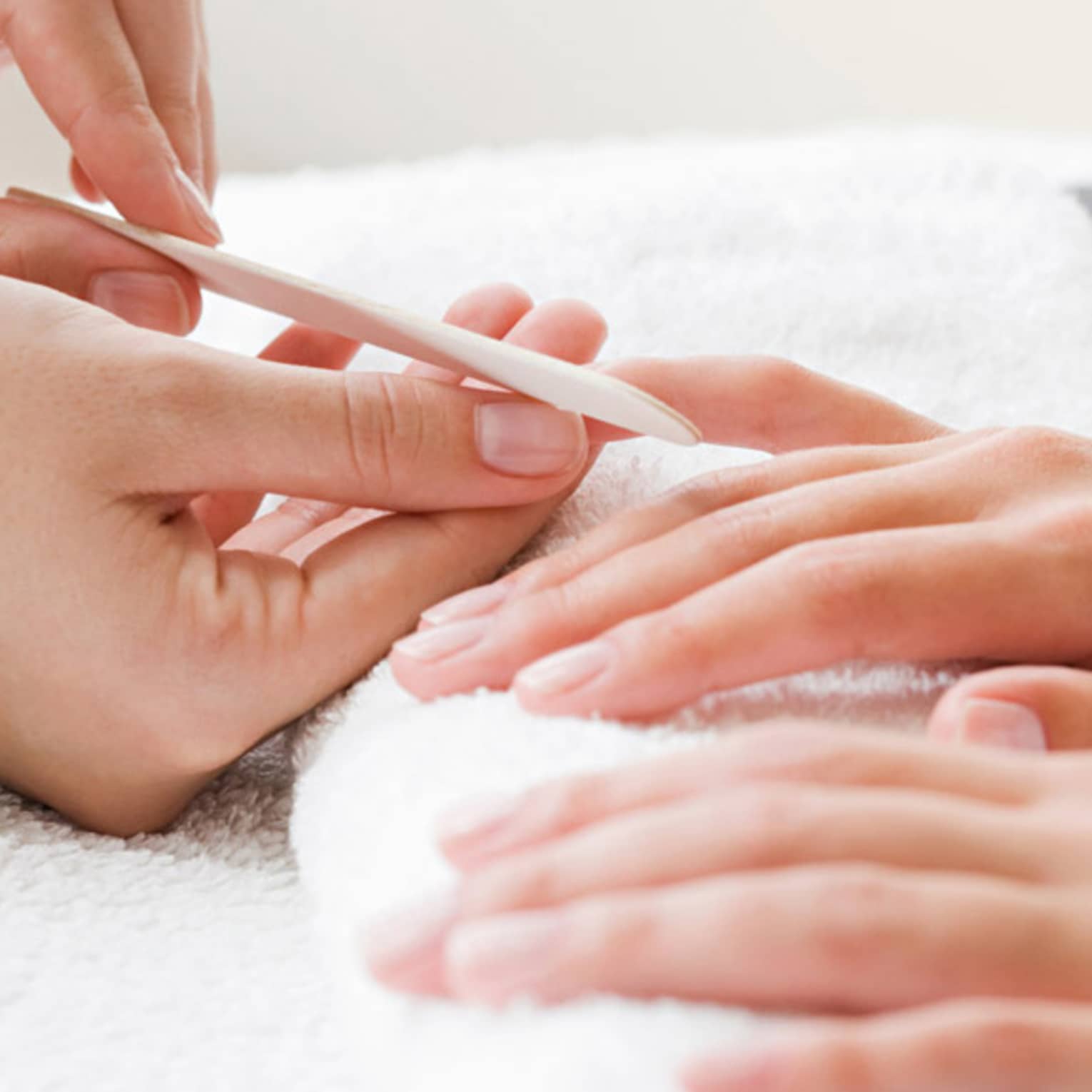 Close-up of spa attendant filing nails of woman's hands as they rest on white towel