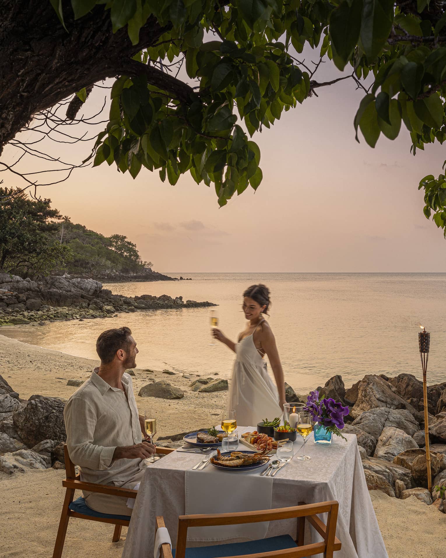 A beach dinner date at dusk, with a couple enjoying a serene seaside view.