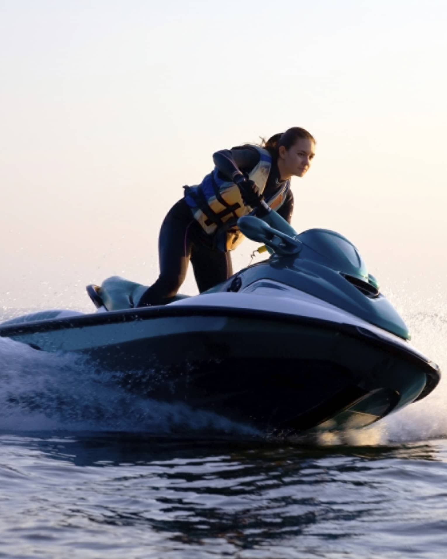Woman wearing life jacket stands, steers jet ski on ocean at sunset