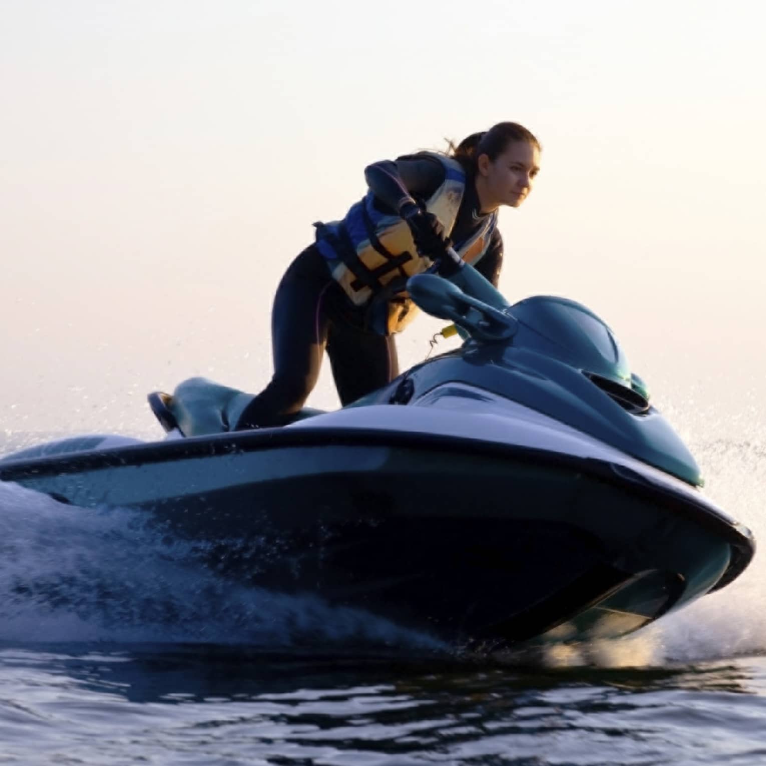 Woman wearing life jacket stands, steers jet ski on ocean at sunset