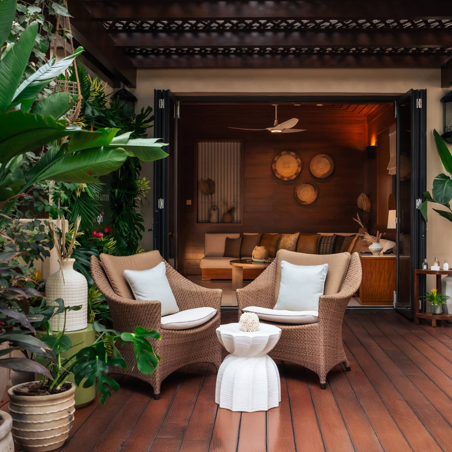 Outdoor deck with hardwood flooring, two rattan chairs with a small table in front surrounded by tropical foliage