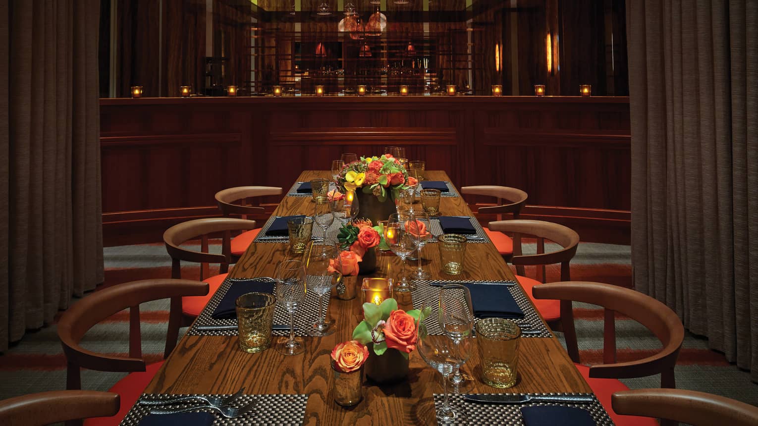 Basket lights hang above a long private dining table with candles, flowers and place-settings 