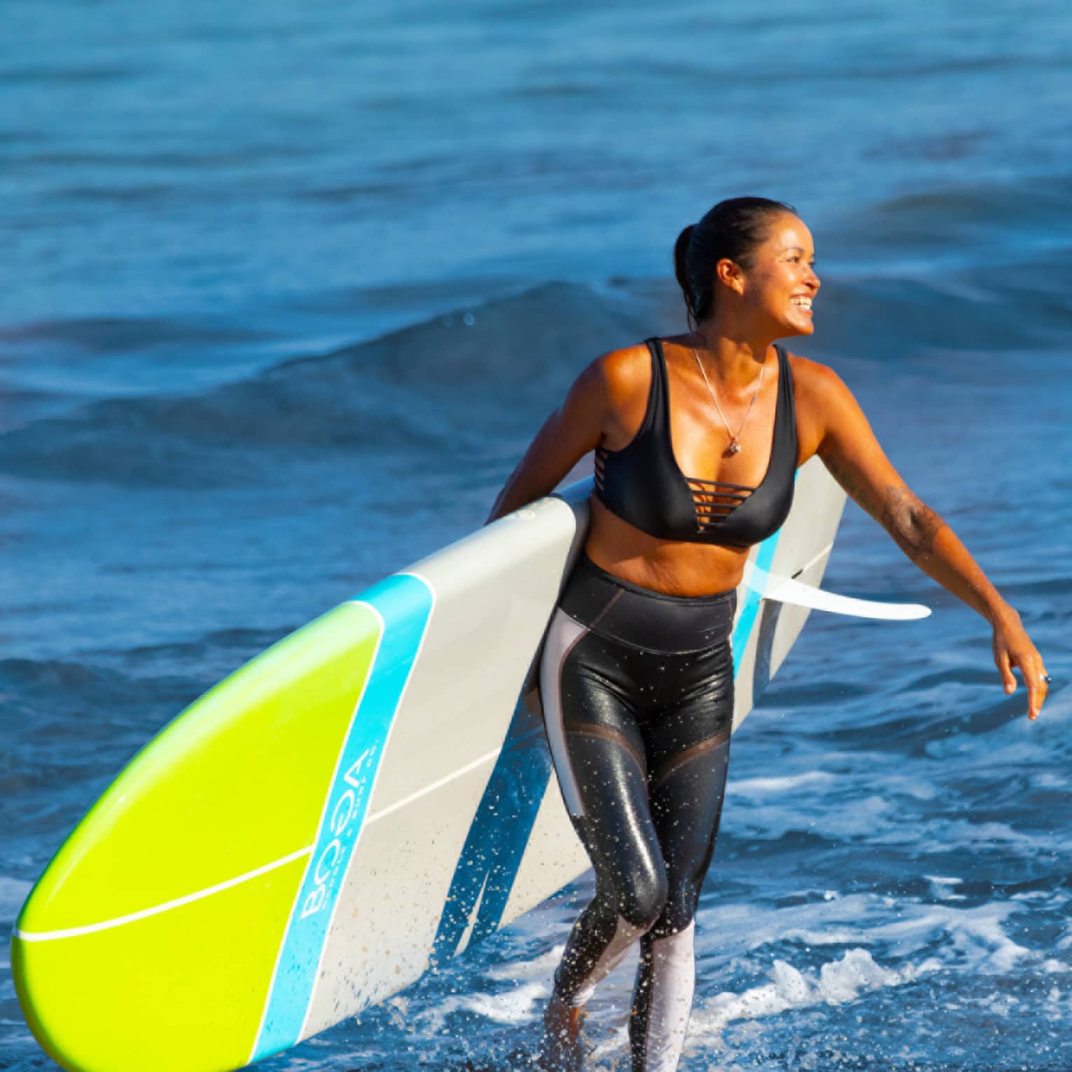 Person walking out of ocean carrying a paddleboard behind back