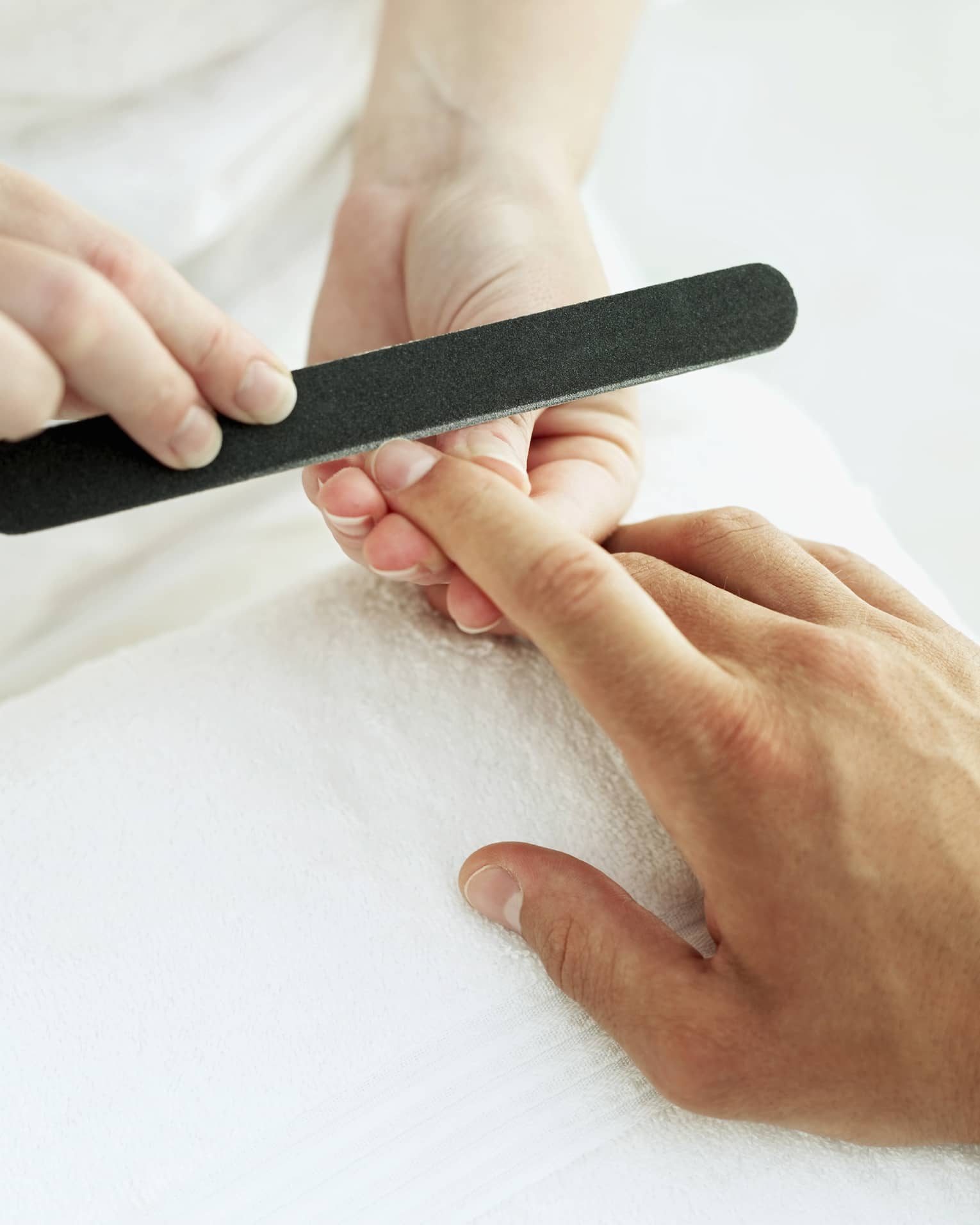 Woman holds manicure nail file to man's fingernails over white towel