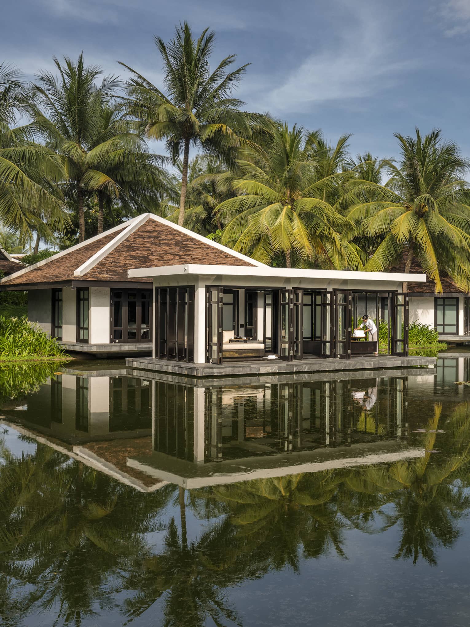 Overwater Heart of Earth spa villa staff folds white towels on deck, reflection in water