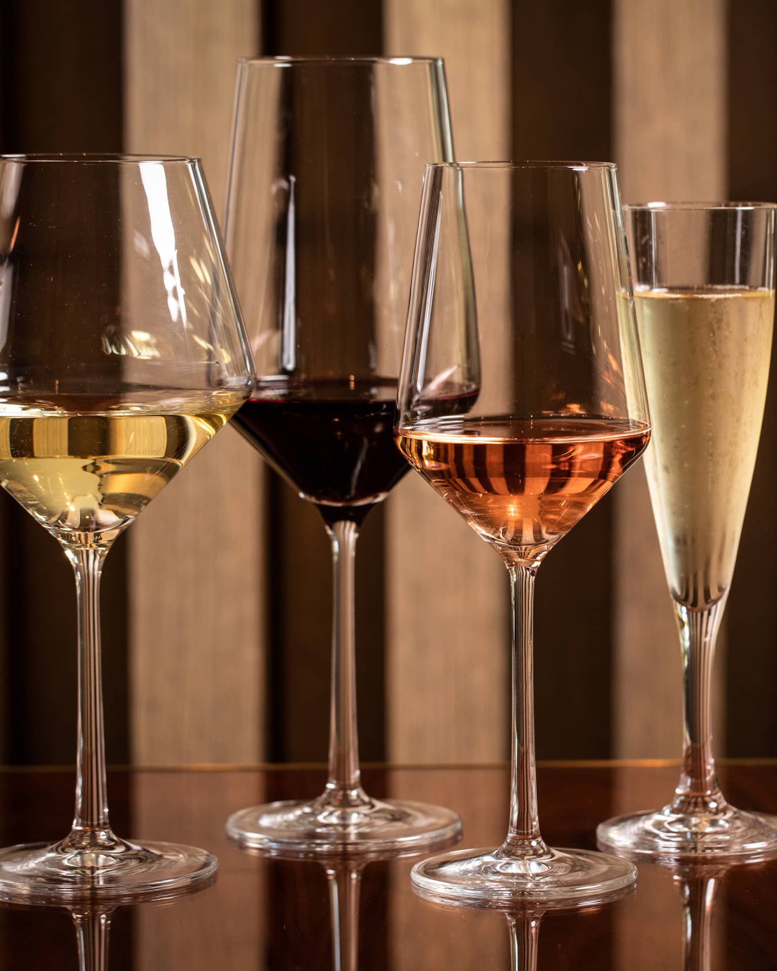 Four modern wine glasses holding white, red and rose wine are lined up on a wooden table
