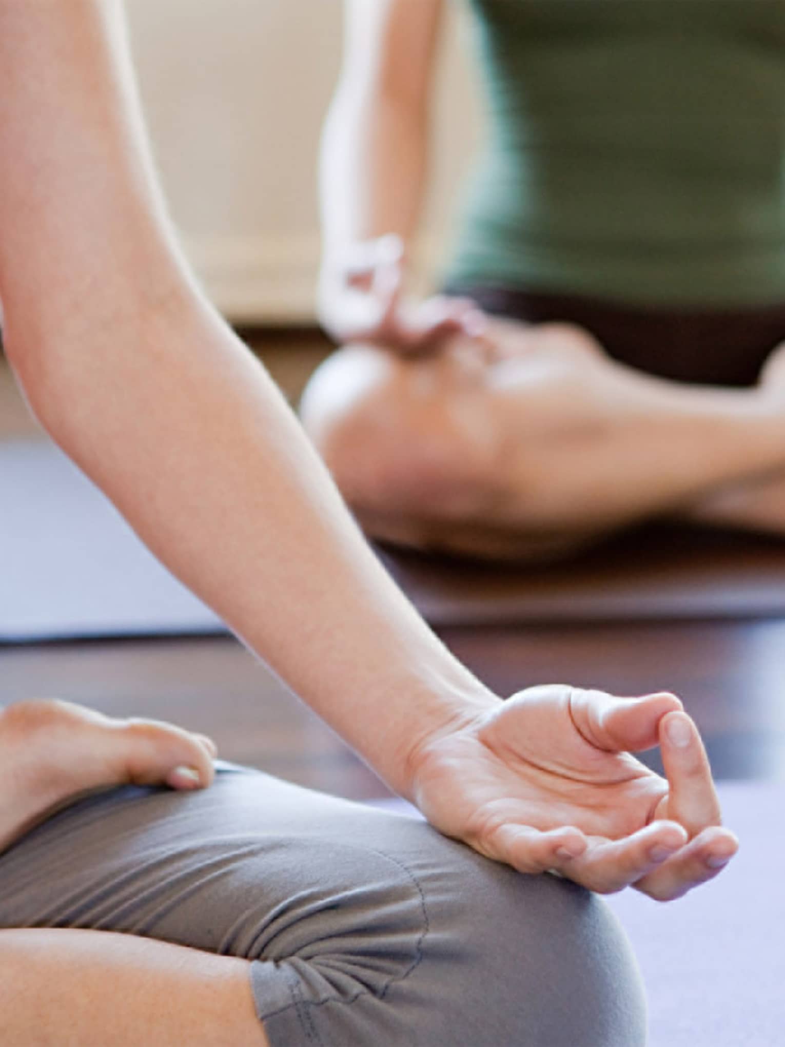 Lower view of two people in workout clothes crossing their legs with hands on knees in yoga pose
