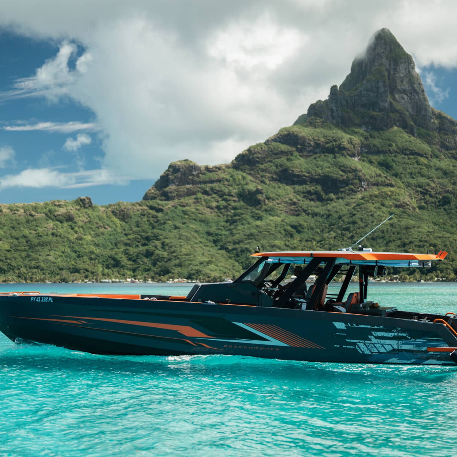 An orange and black yacht charter boar sails in front of a mountain landscape