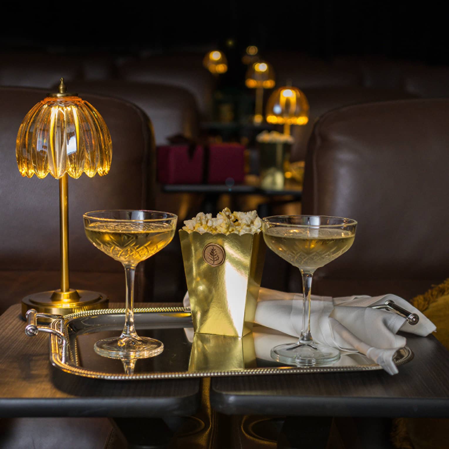 Two filled coupe glasses on a silver serving tray with popcorn in front of a golden dome light.