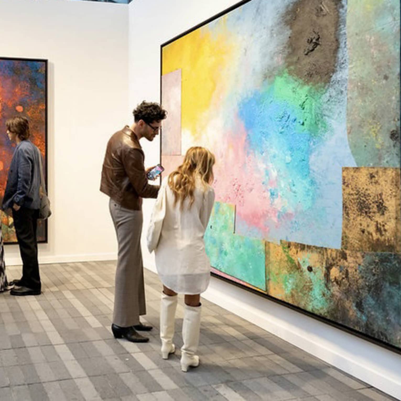 People observing large paintings at an art gallery