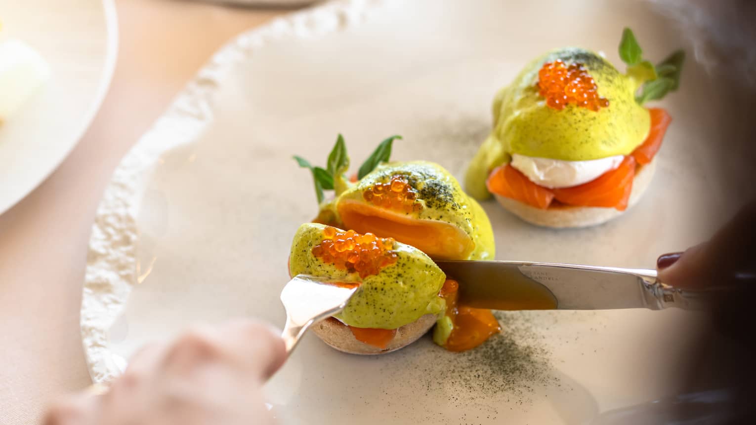 A guest uses a fork and knife to cut a colourful food item on a decorative oval-shaped white plate.