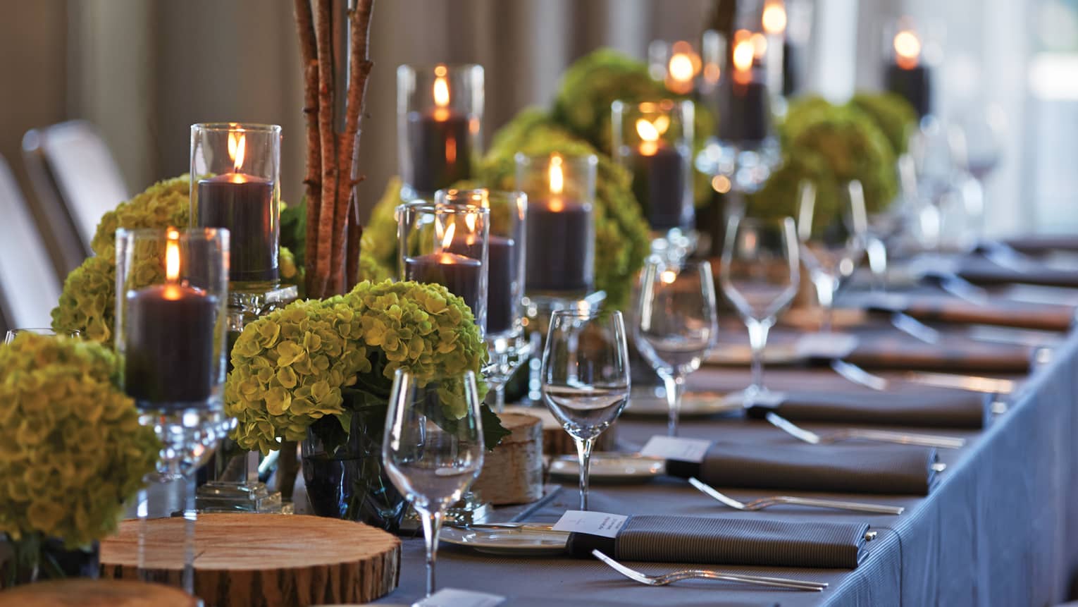 Black pillar candles in votives, green flowers, wine glasses along banquet table