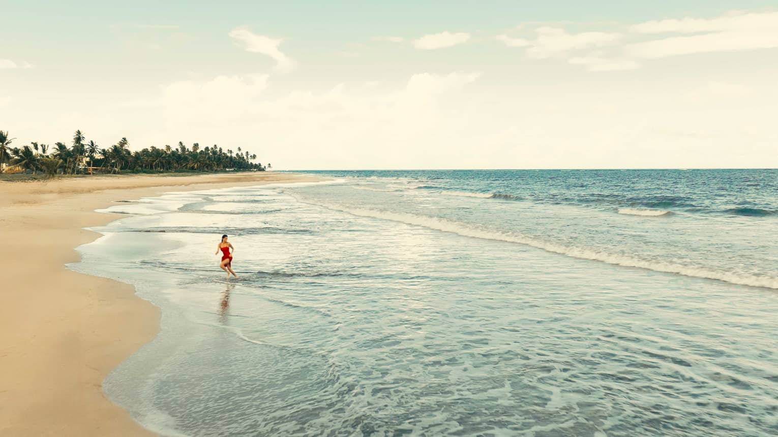 A person runs through the lapping water on a tropical beach