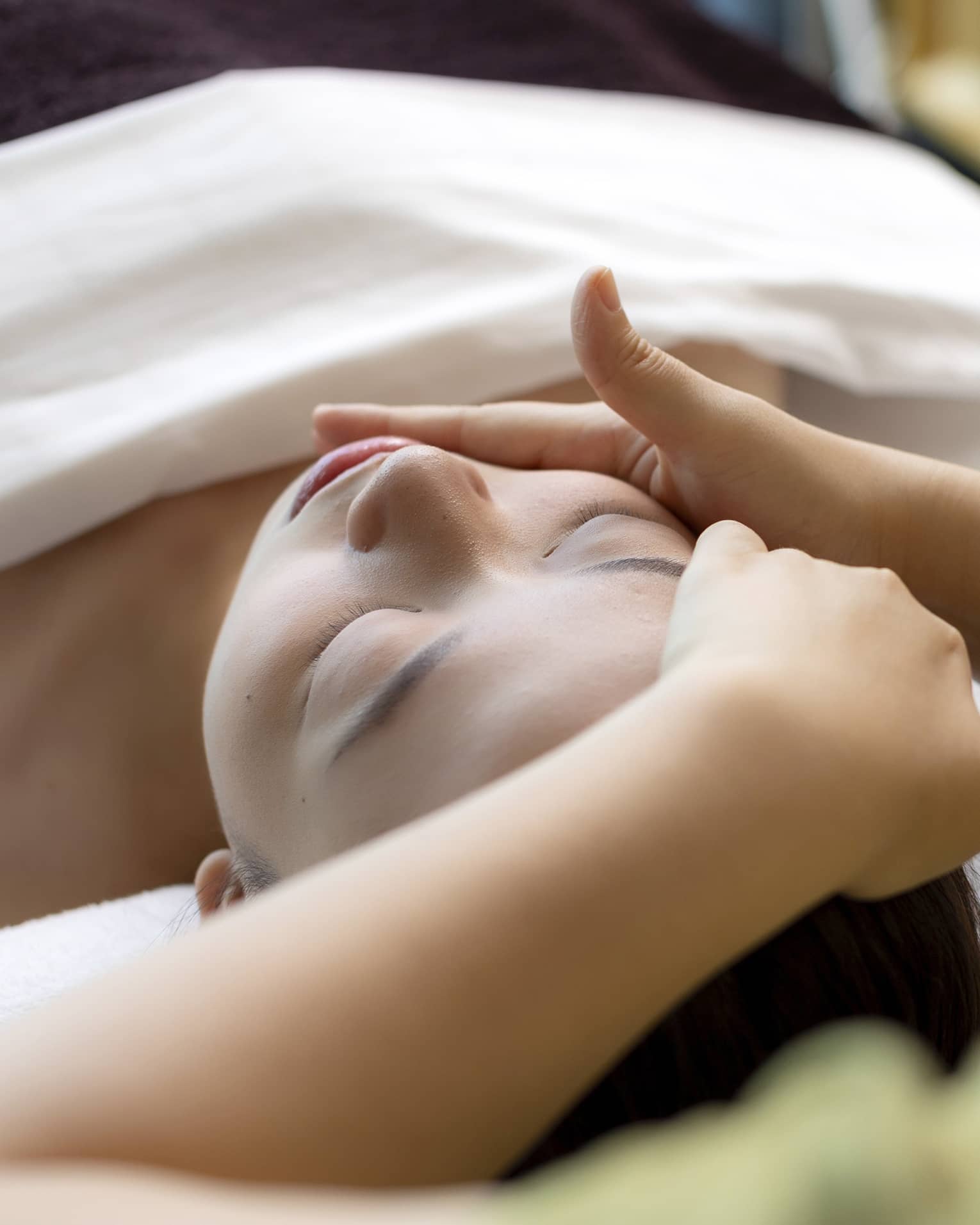 Hua Spa staff massages woman's face as she lays on treatment table