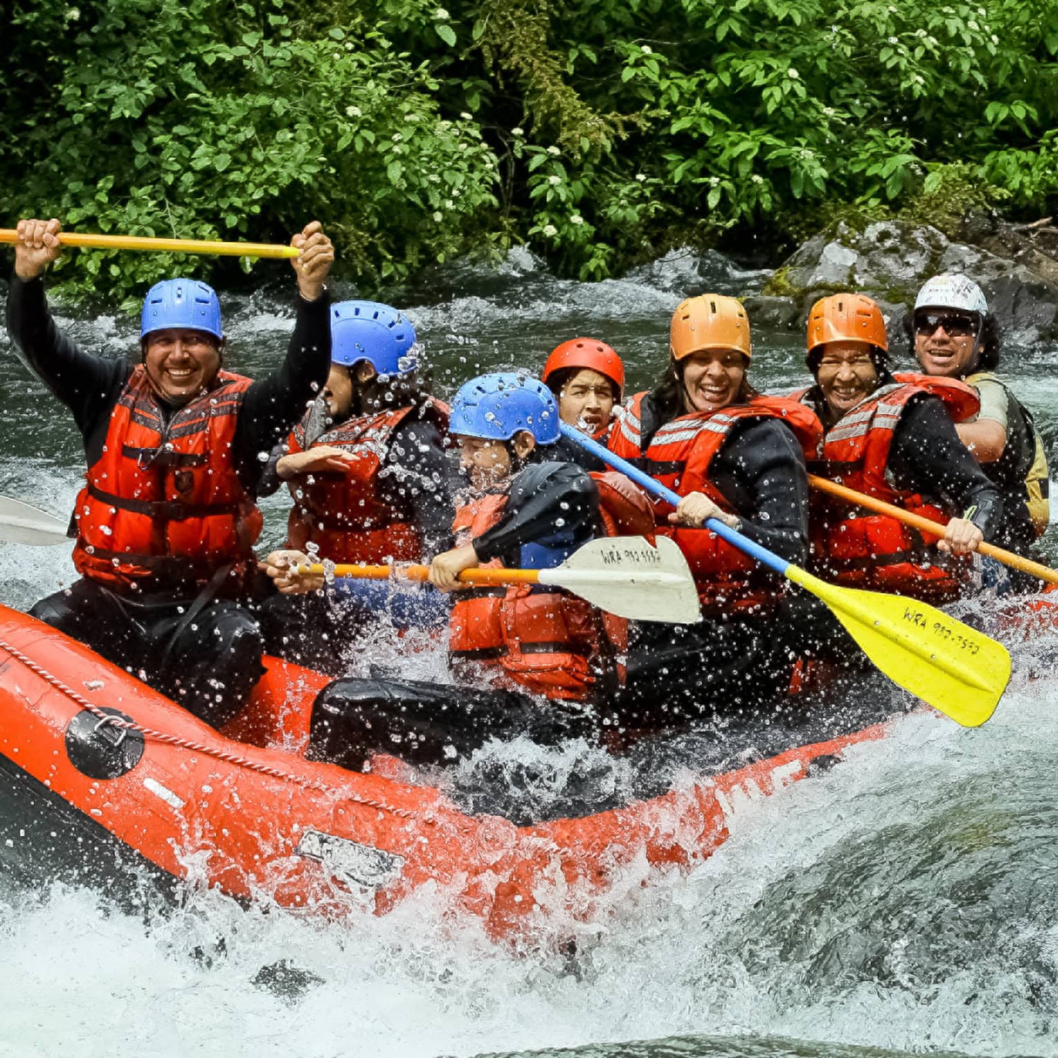 Smiling family wearing life jackets, helmets on white water raft on river rapids 