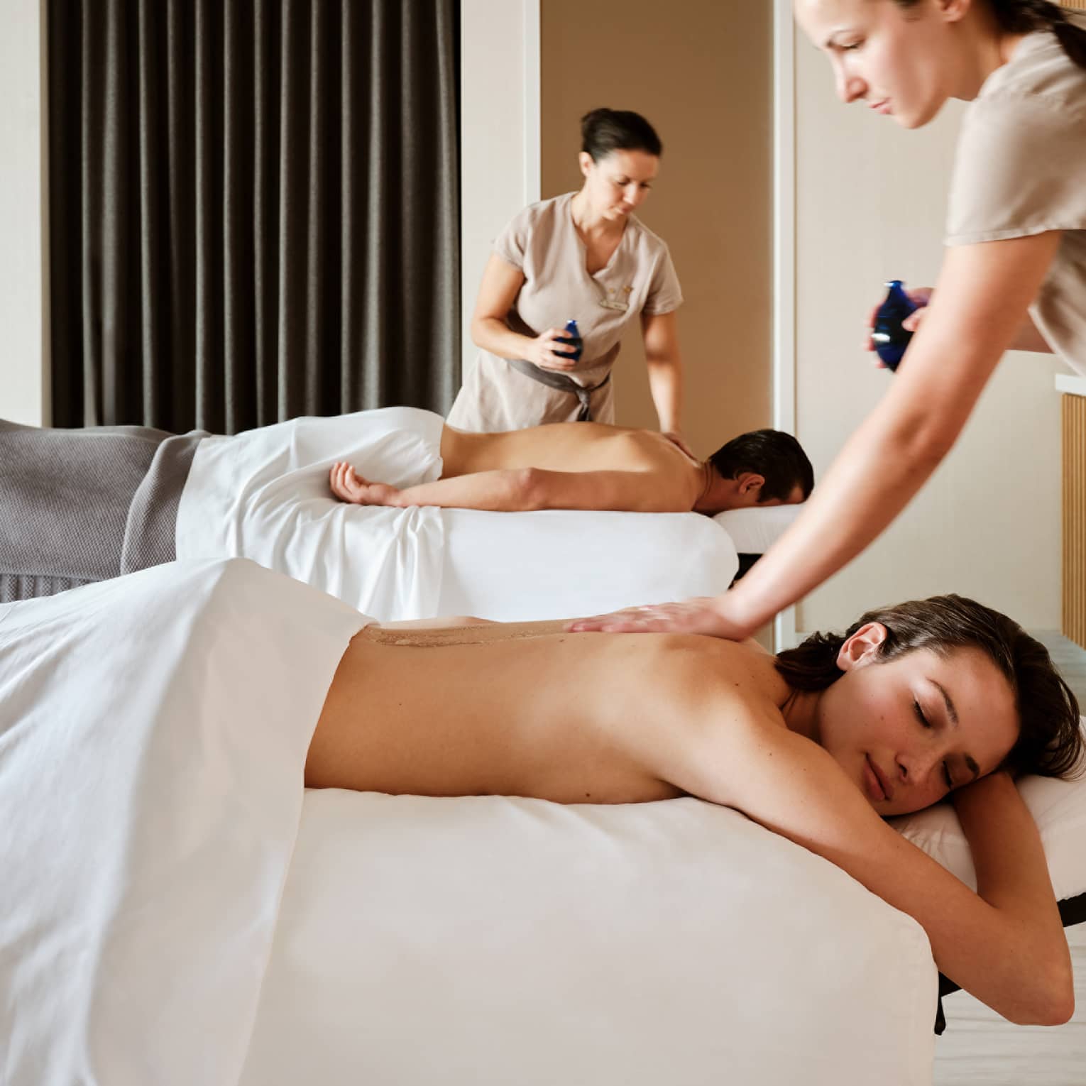 Couple lying prone on spa tables while being massage by spa therapists