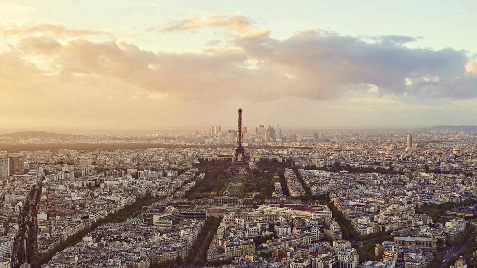 Sweeping city view of Paris rooftops, buildings, Eiffel tower at sunset