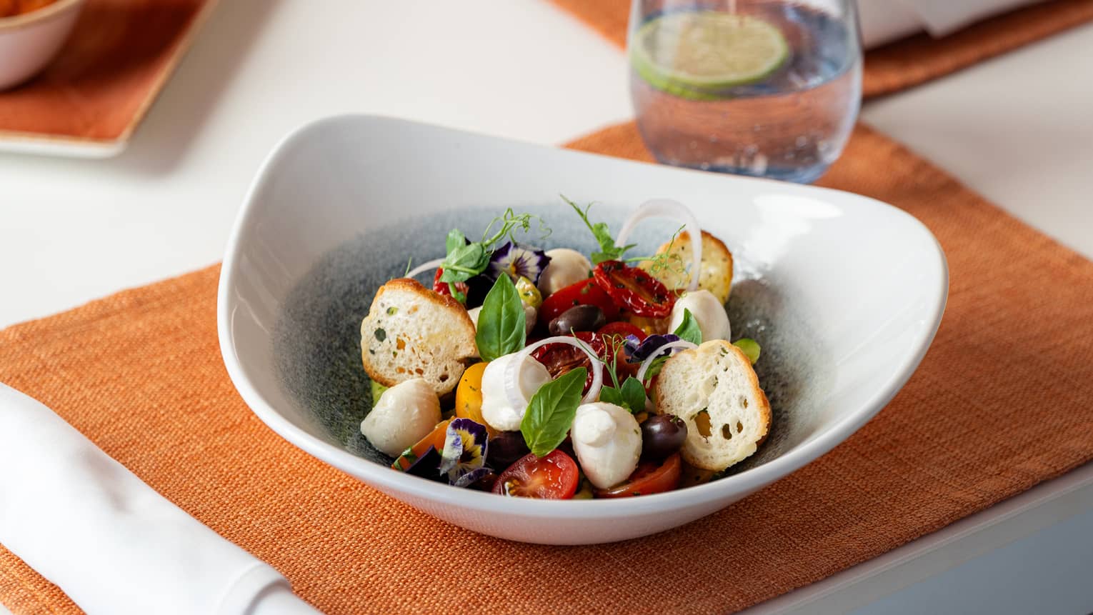 Baby Buffalo Cheese, Heirloom Cherry Tomato, Cucumber, Olive, Basil Pesto, Balsamic, Red Onion, Herbs Crouton served in a white bowl