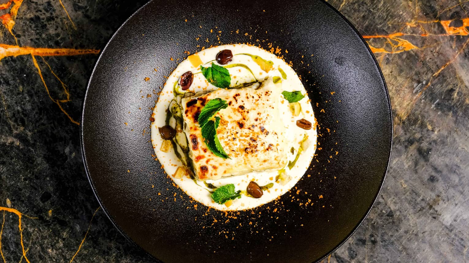 Millefoglie di pasta fresca ai Carcio cream with garnish in black dish on marble counter