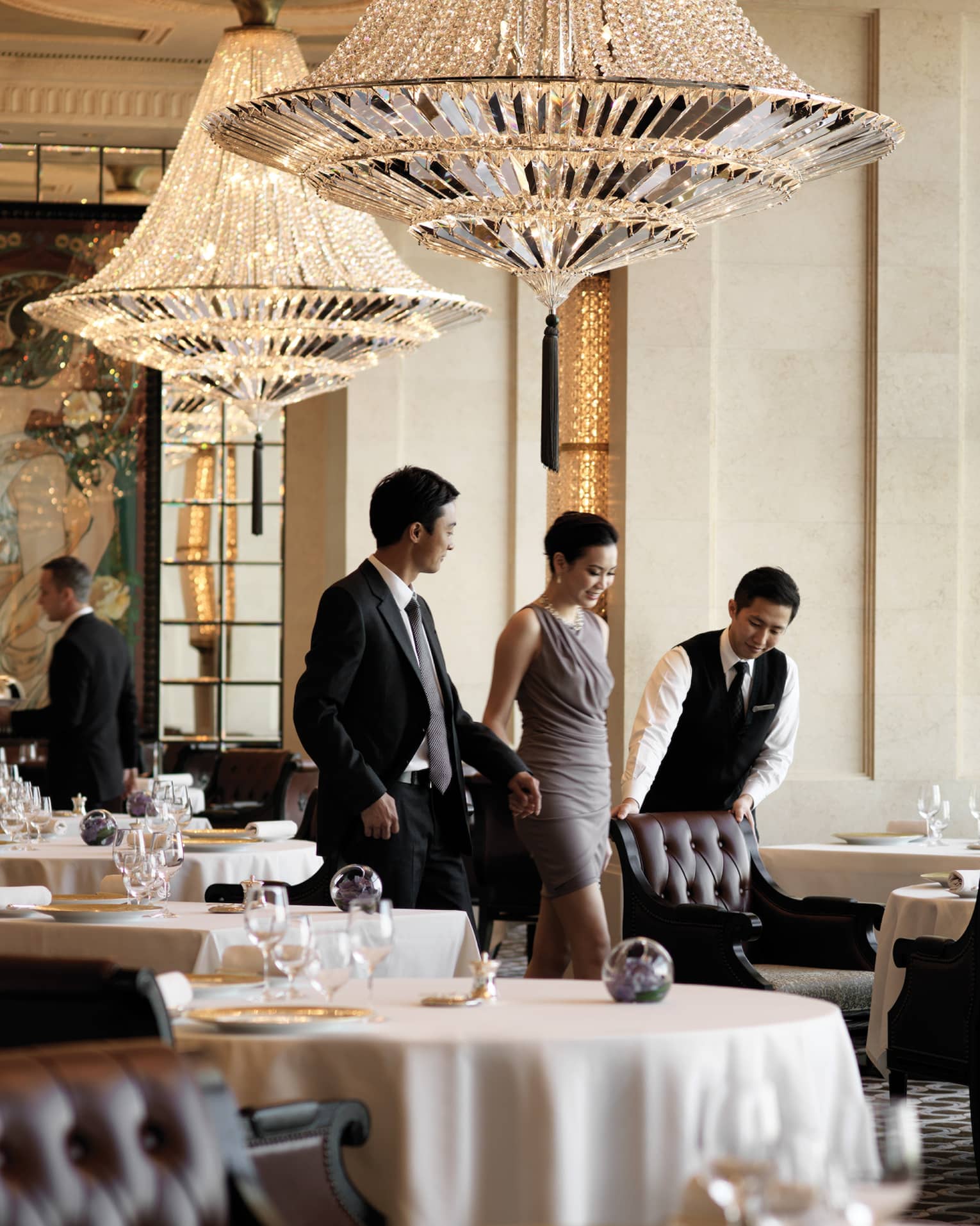 A male waiter pulls a leather seat out at a dining table for a woman